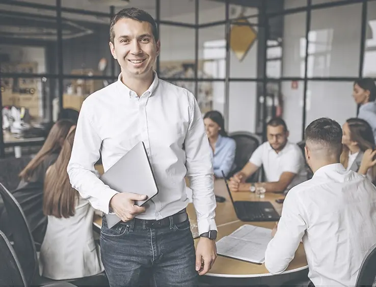 Asesor de Te Ayudamos a Negociar sonriendo en la oficina, con el equipo trabajando detrás